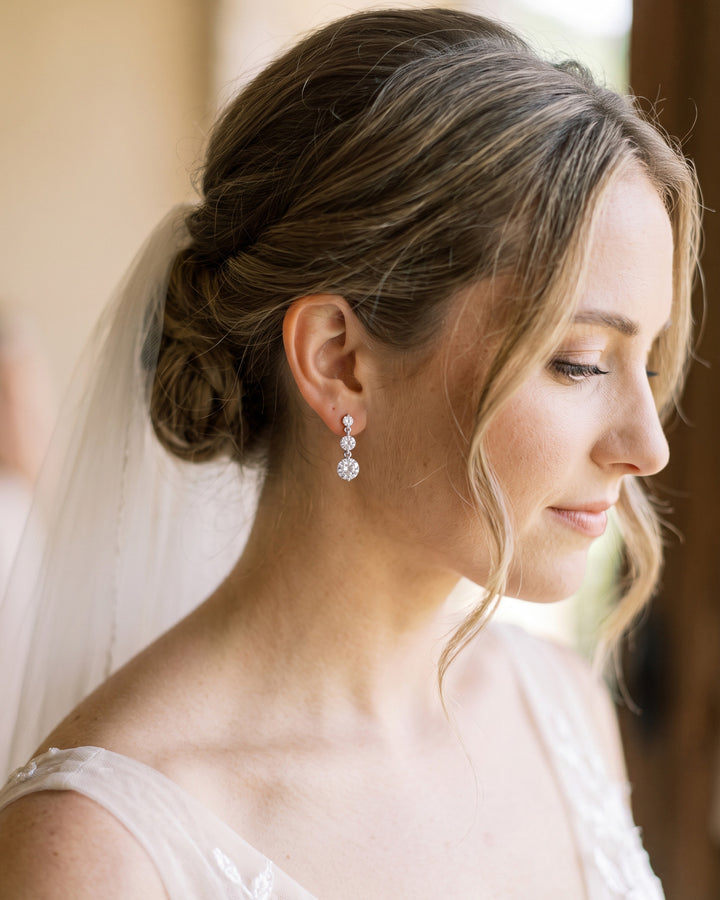 Bride in a veil wearing Nadia drop earrings by a window