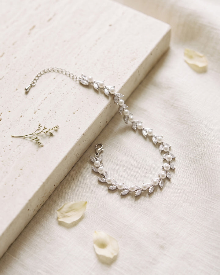 Sydney Pearl bracelet draped over travertine stone on ivory linen with petals