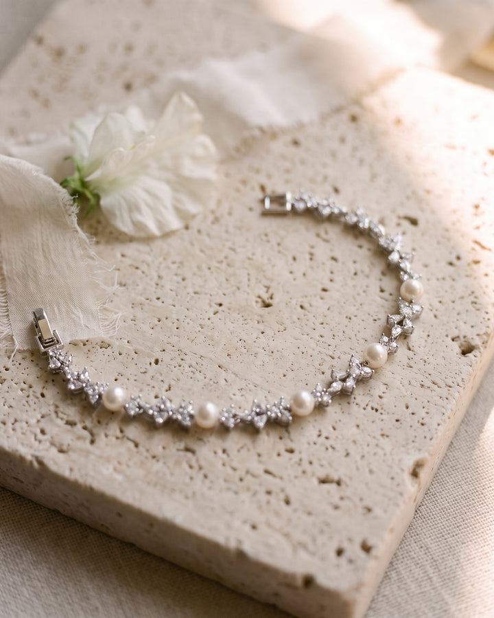 Kelsey pearl bracelet laid on travertine stone with a white flower