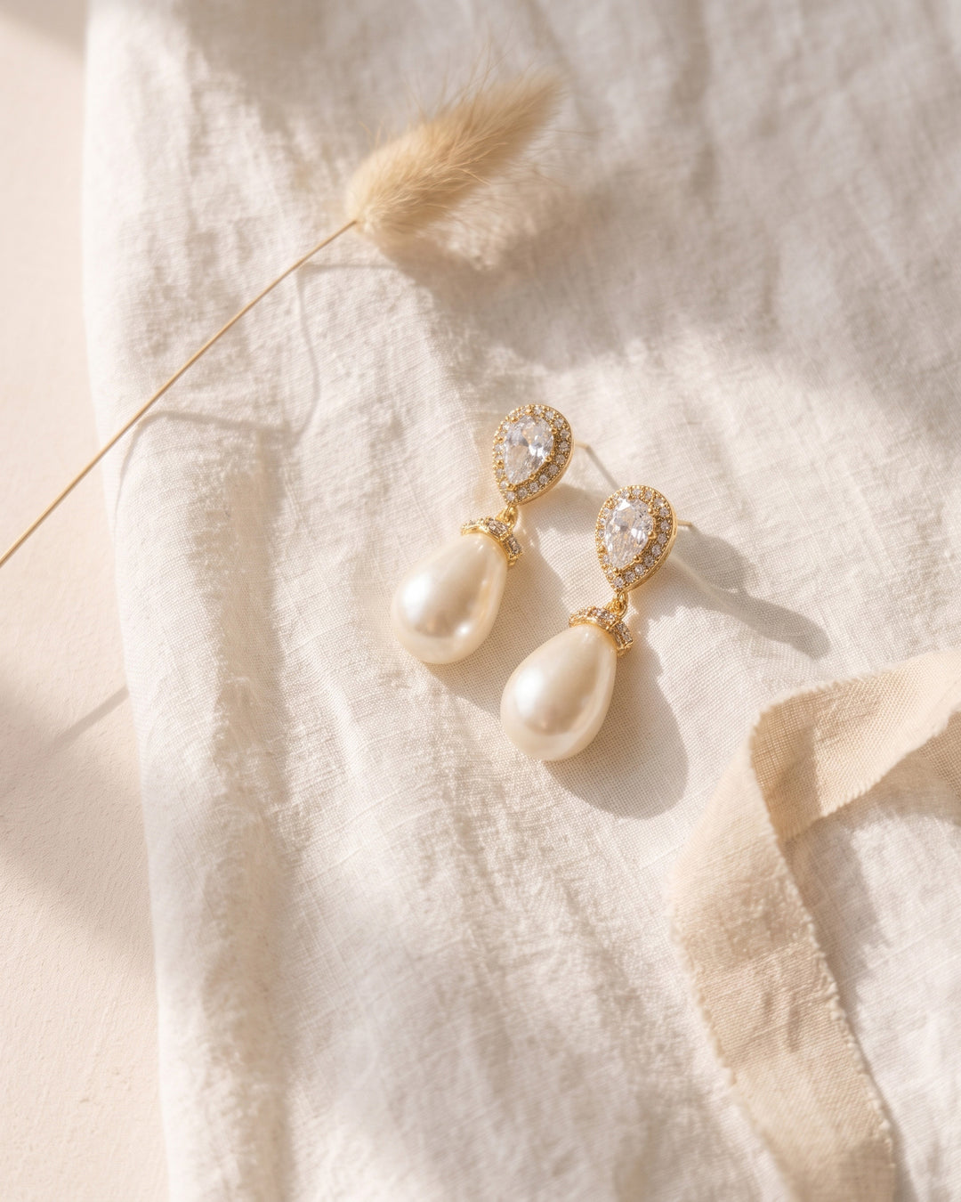 Gold Nina earrings with teardrop pearls on ivory linen with bunny-tail grass