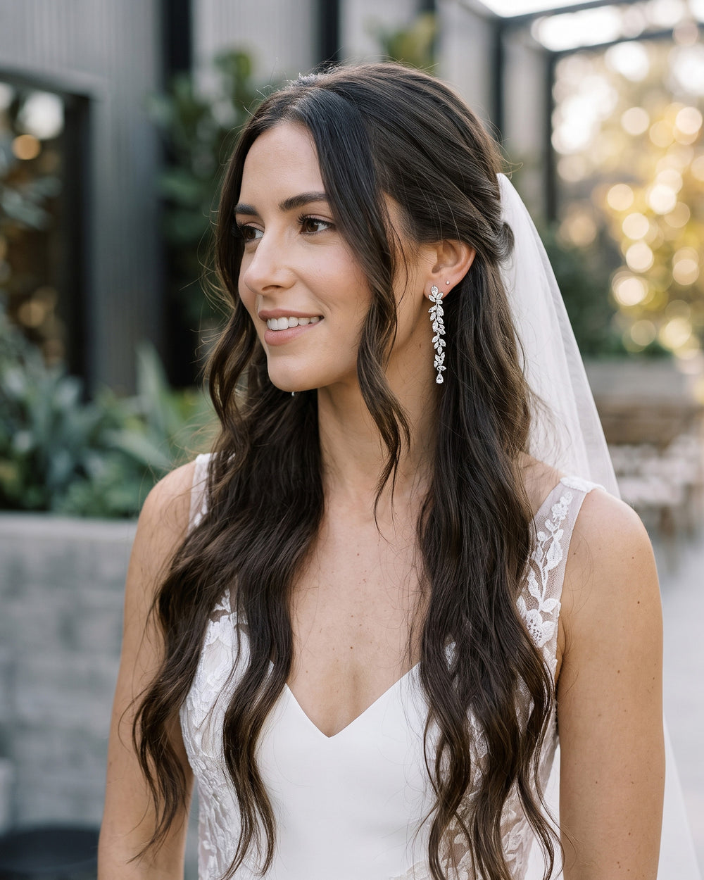 Bride with long dark waves and a veil wearing the Anastasia wedding earrings outdoors
