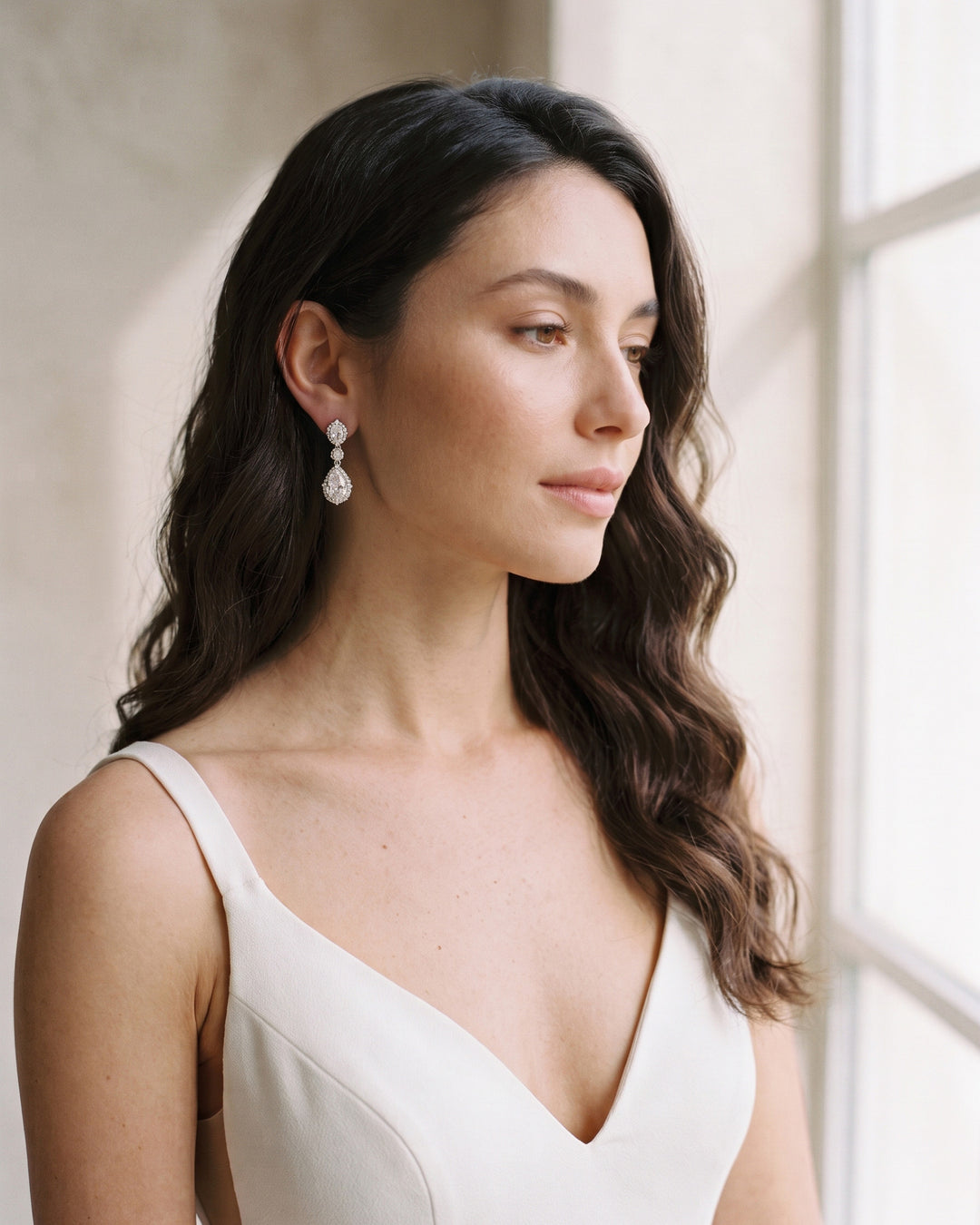 Bride in a V-neck gown by a window wearing the Emerson vintage-inspired drop earrings