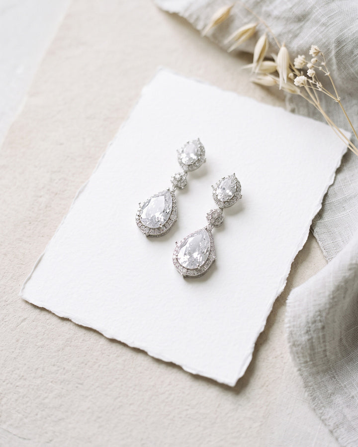 Emerson halo earrings on deckle-edge paper with dried flowers, showing the pear drop