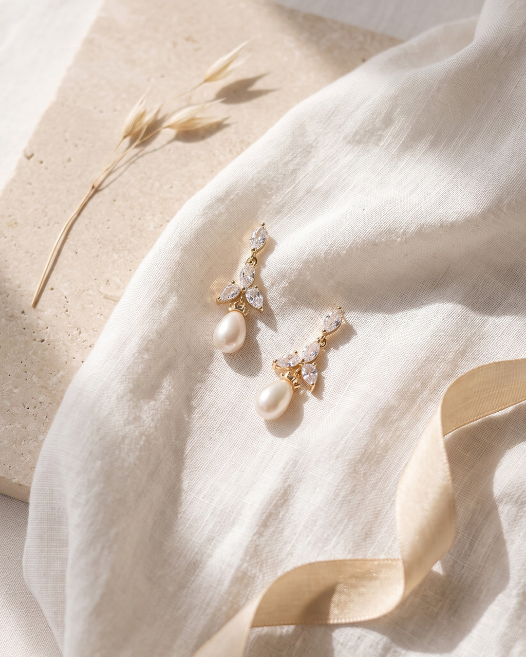 Gold Olivia earrings on linen and stone showing the freshwater pearl drops and CZ petals up close