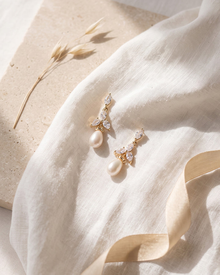 Gold Olivia earrings on linen and stone showing the freshwater pearl drops and CZ petals up close