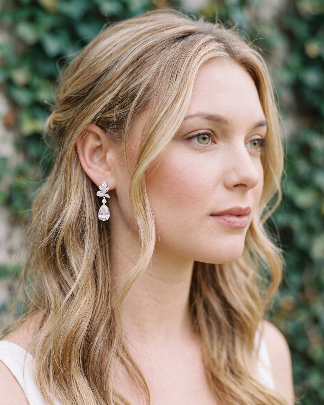 Bride with half-up blonde waves wearing the Madison CZ teardrop earrings by an ivy wall