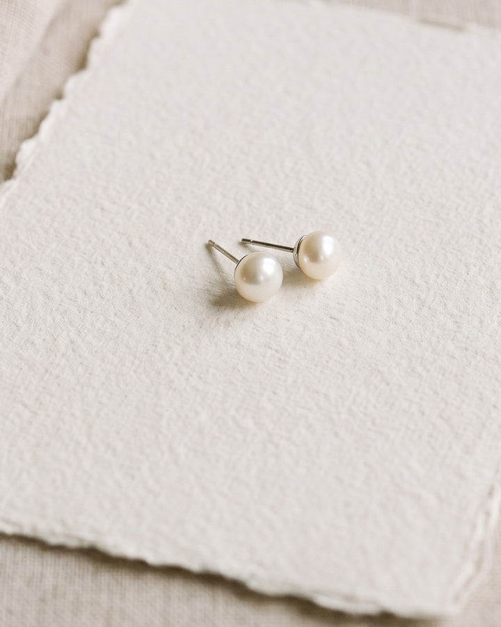 Pair of 8mm pearl wedding studs resting on deckle-edge paper