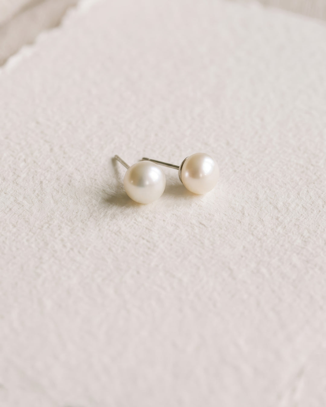 Classic pearl stud earrings with round light ivory pearls on textured ivory paper