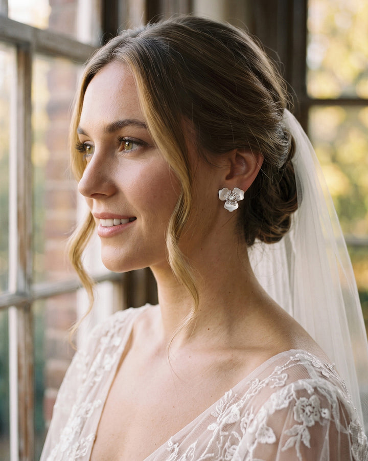Bride with a veil and low updo wearing Kacie flower studs by a sunlit window