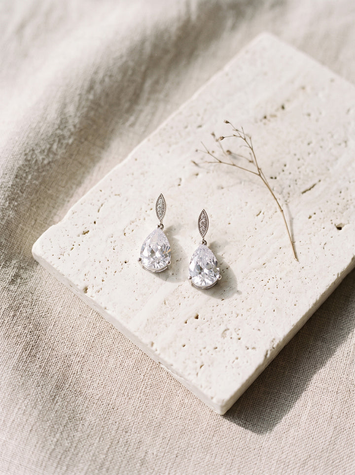 Callie CZ earrings on travertine stone over soft linen with a dried stem