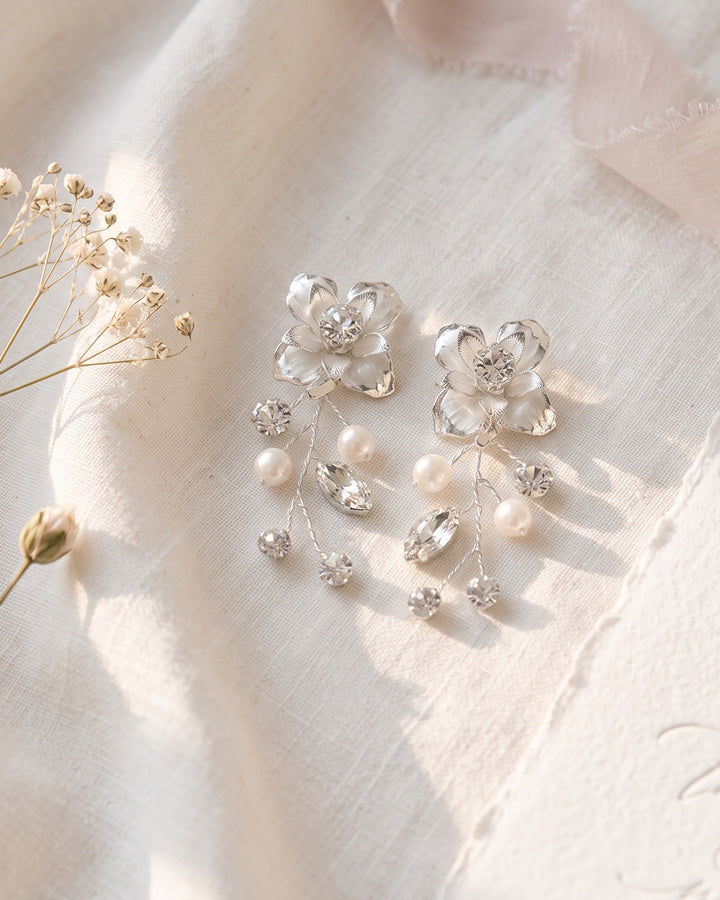 Silver floral pearl earrings laid on ivory linen with baby's breath
