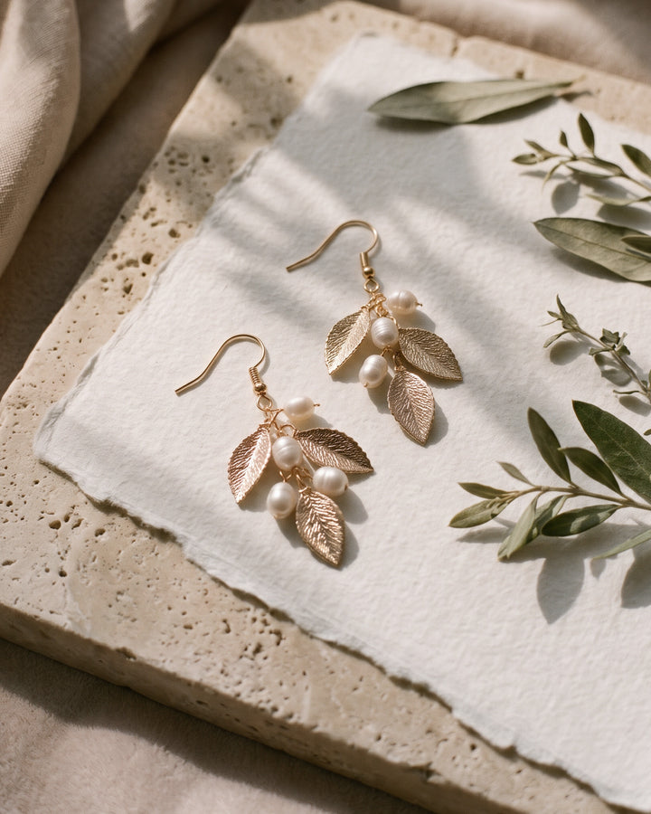 Nola gold leaf earrings with freshwater pearls on stone and paper beside fresh greenery