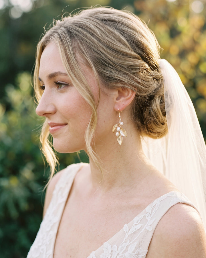 Profile of a bride in a lace gown and veil wearing the Nola gold leaf drop earrings