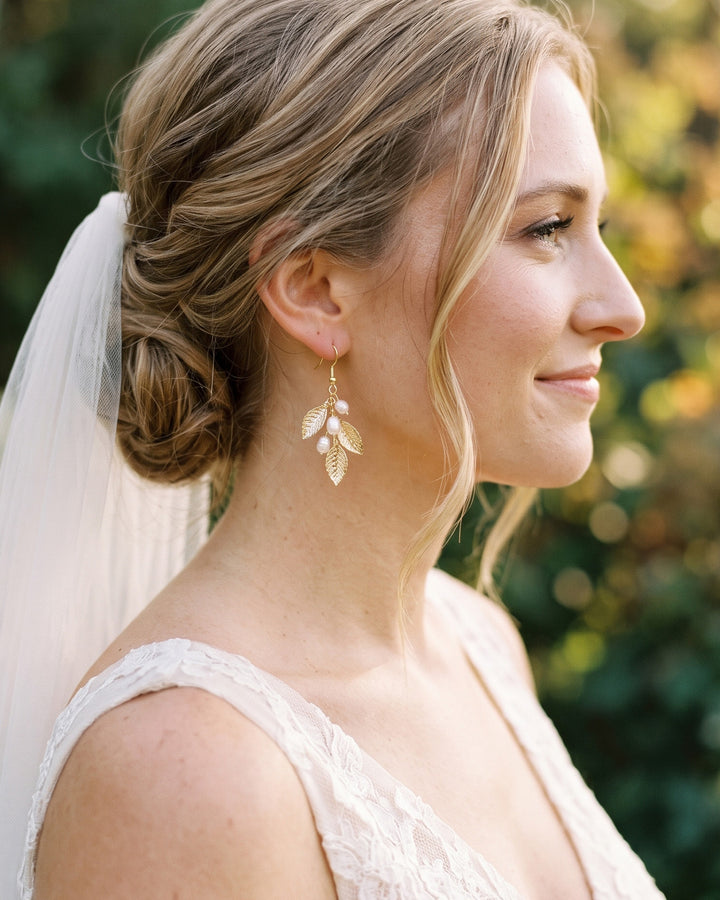 Bride with a veil and low updo wearing the Nola gold leaf and pearl wedding earrings