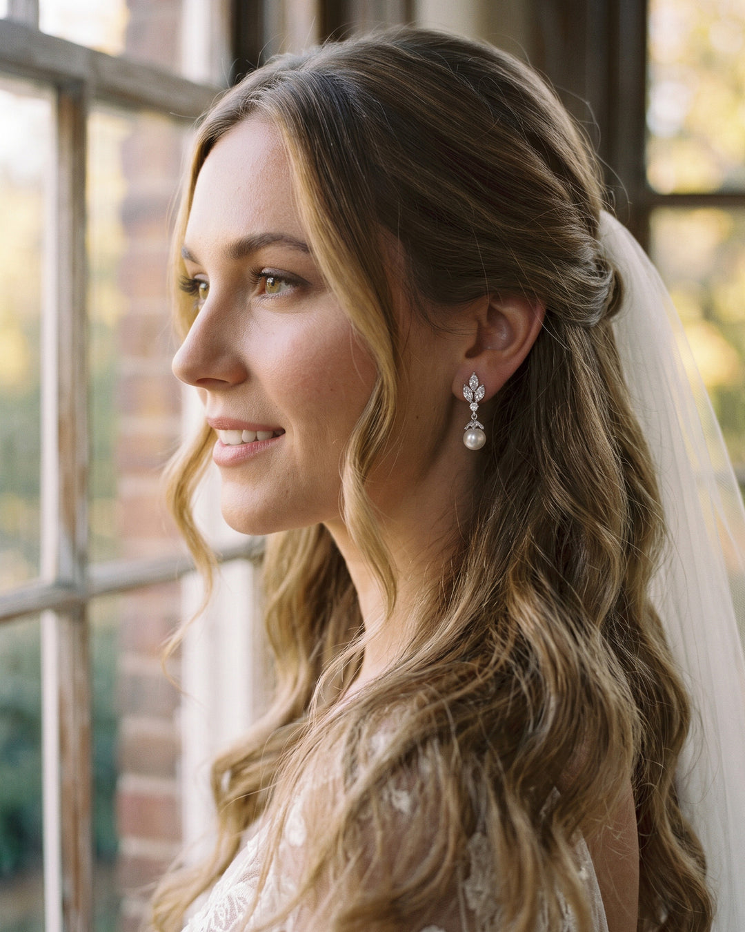 Bride with long waves and a veil wearing Bethany pearl drop earrings by a window
