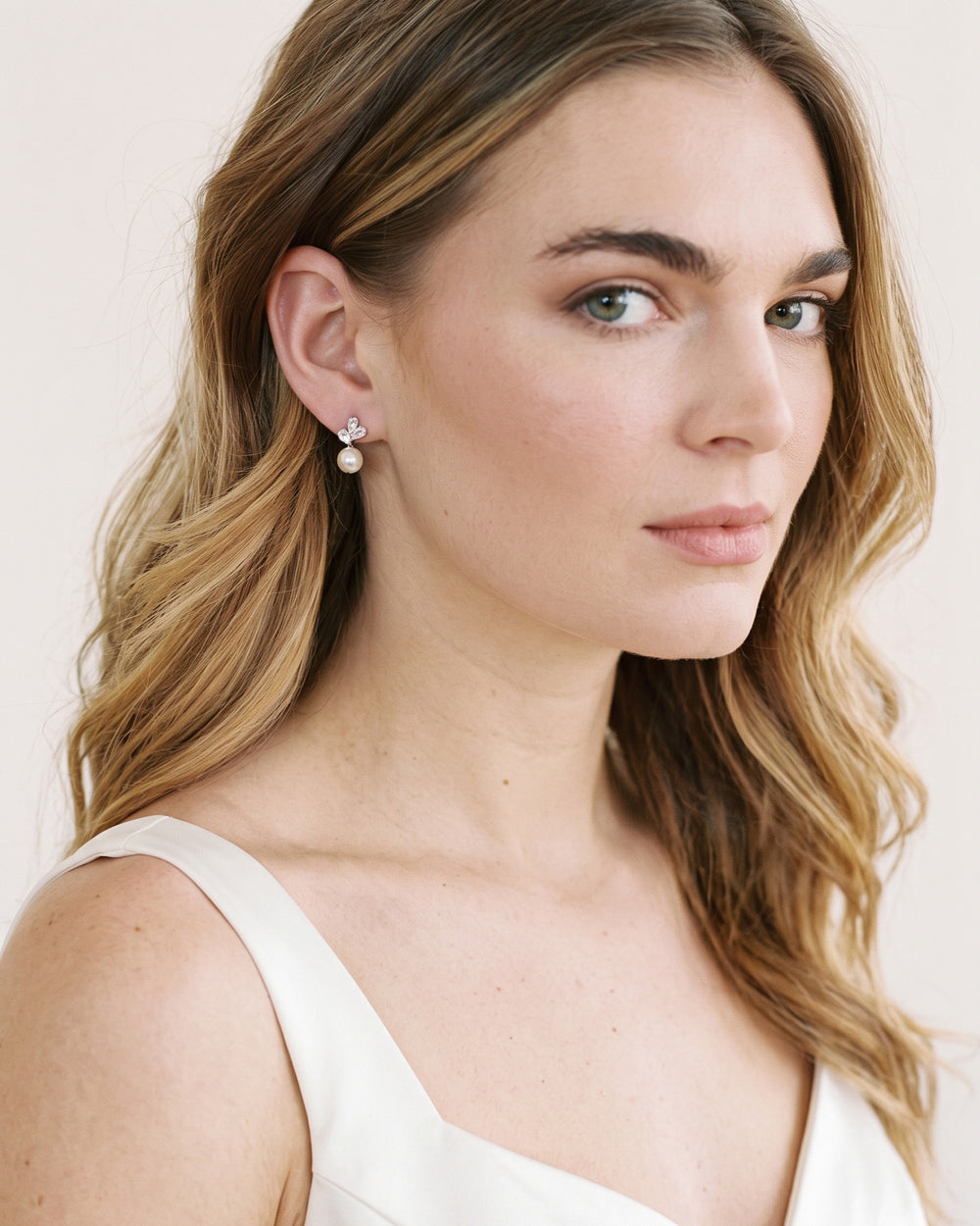 Bride with soft blonde waves in a white tank wearing dainty Meadow pearl stud earrings