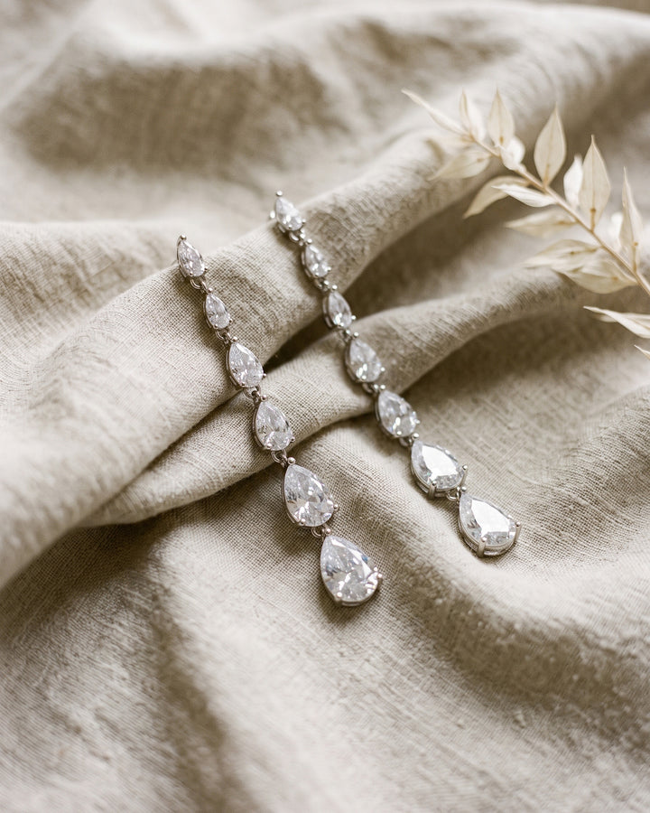 Celine cubic zirconia drop earrings laid on natural linen beside dried grasses