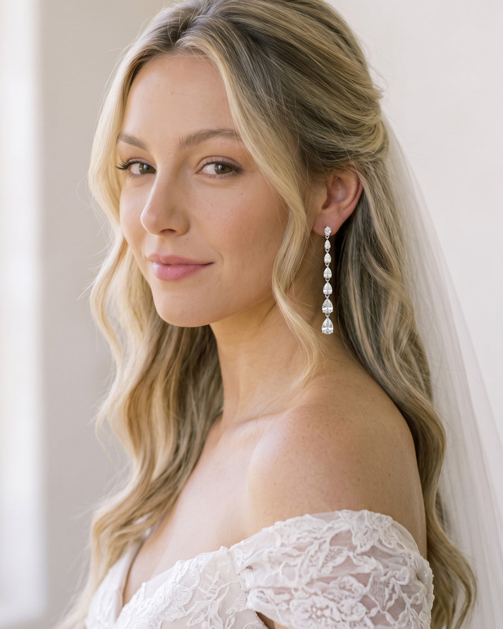 Blonde bride with soft waves and a veil wearing long Celine pear CZ statement earrings