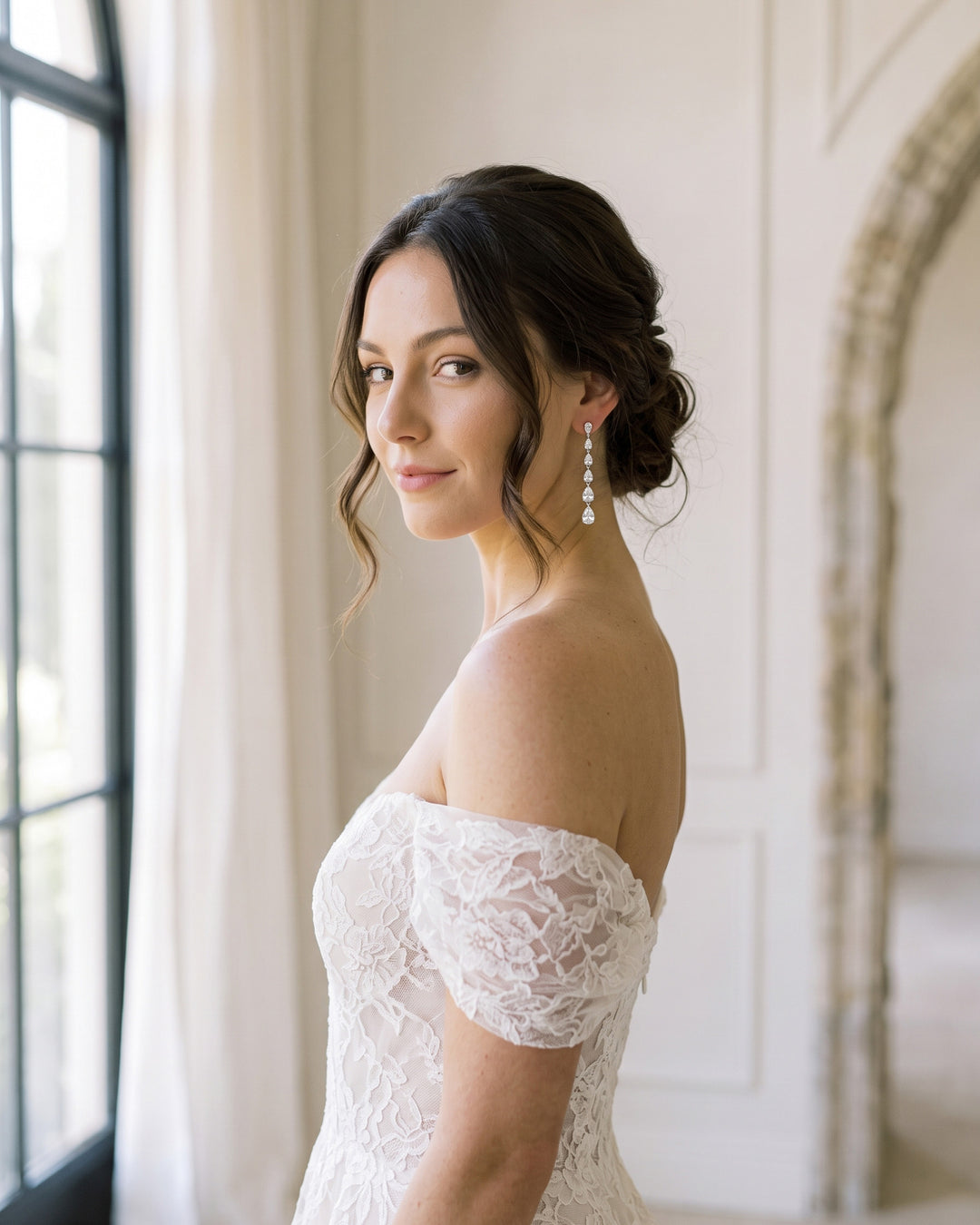 Brunette bride in an off-the-shoulder lace gown with an updo and Celine long CZ earrings
