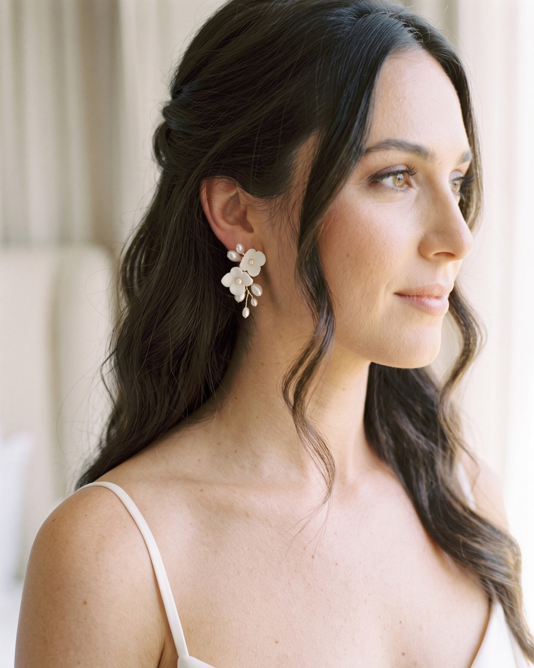 Bride with half-up waves wearing the Kara pearl flower earrings in soft window light