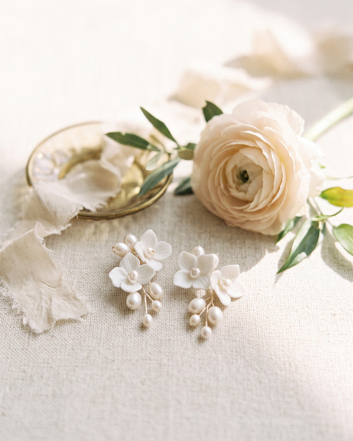 Kara pearl and flower earrings on ivory linen beside a pale ranunculus