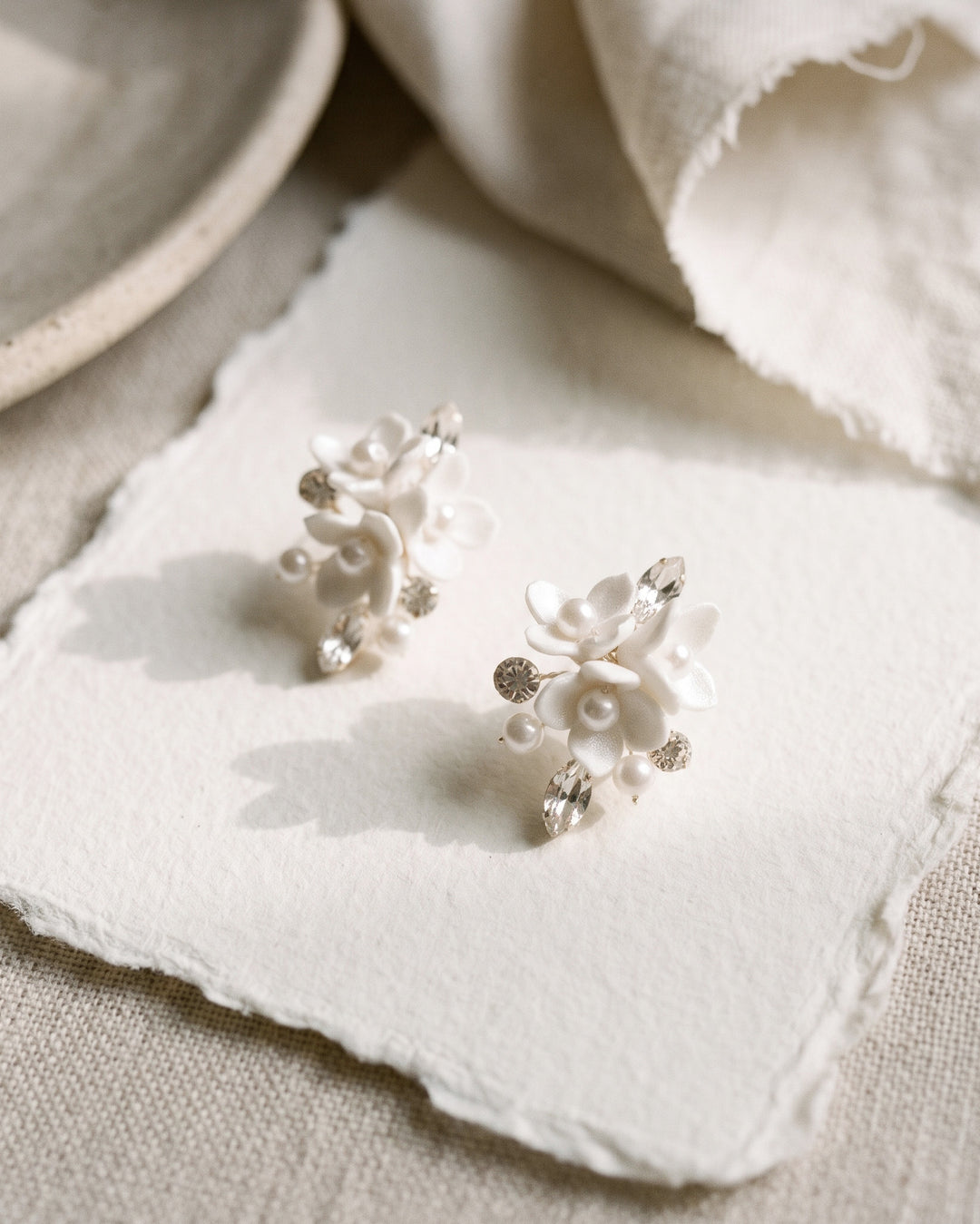 Elin wedding earrings styled on handmade paper, showing the ivory flower and pearl clusters