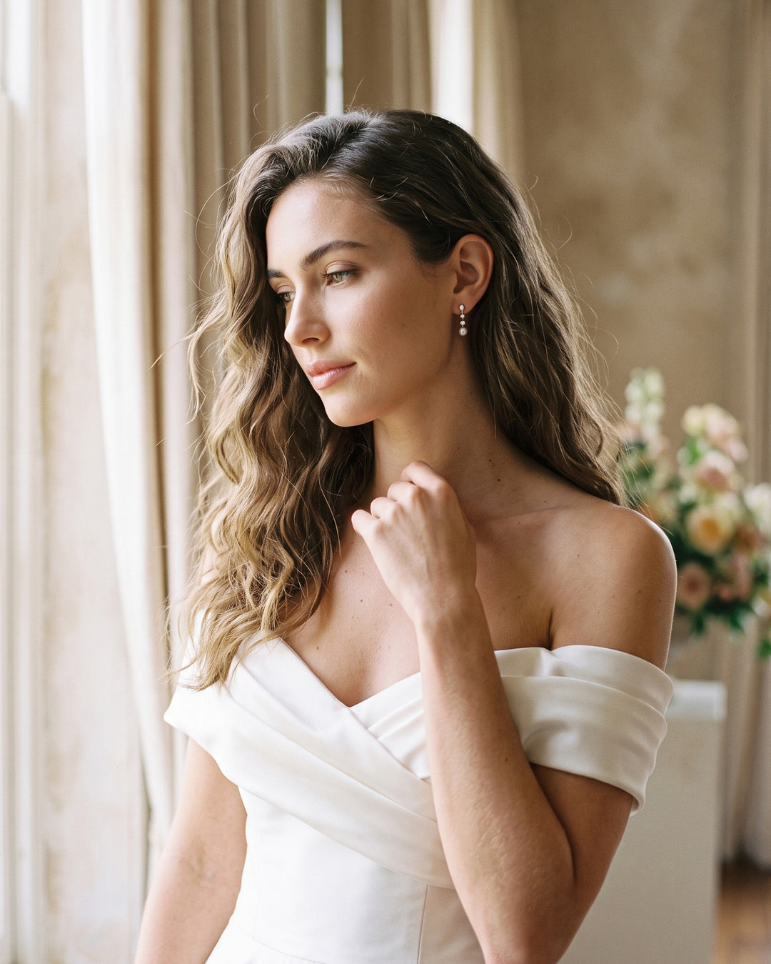 Bride in an off-shoulder gown by a window wearing Bailey pearl drop earrings