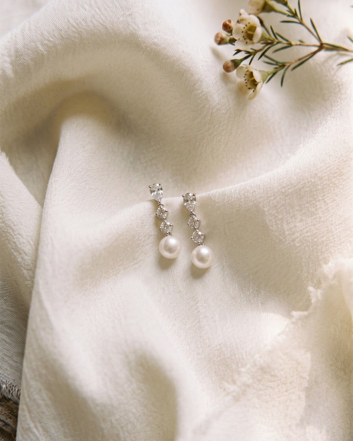 Bailey pearl drop earrings resting on ivory fabric with small white flowers