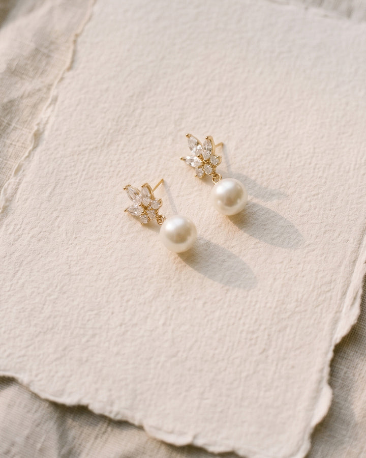 Gold Peyton wedding earrings with light ivory pearls and marquise stones resting on handmade cream paper