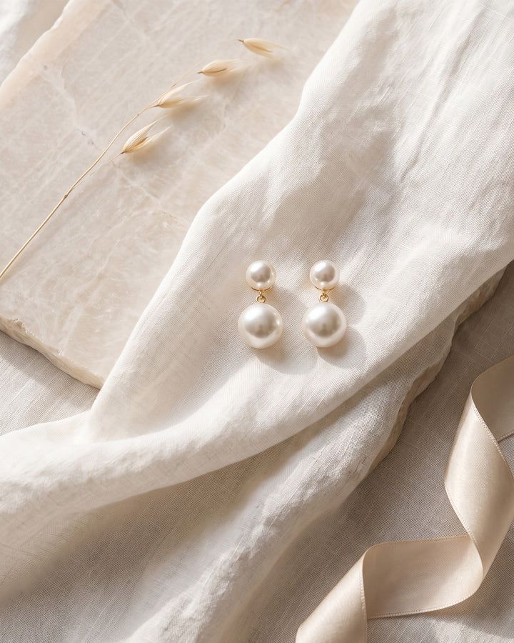 Gold Nadine bridal earrings on linen and stone showing the stacked light ivory pearls