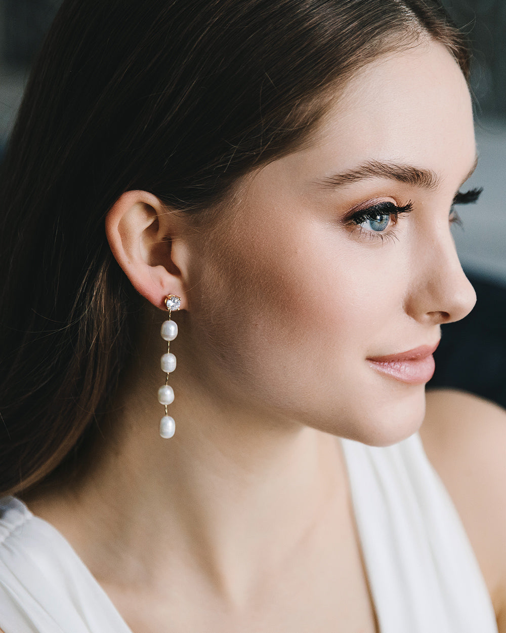 Smiling model in profile wearing Tess long pearl drop wedding earrings