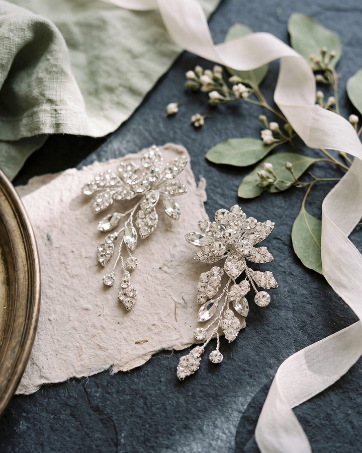 Pair of Marlena earrings on dark slate with greenery, showing the rhinestone leaf detail