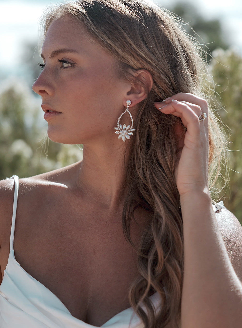 Bride with long waves tucking her hair back to show Marnie pearl and rhinestone hoop earrings