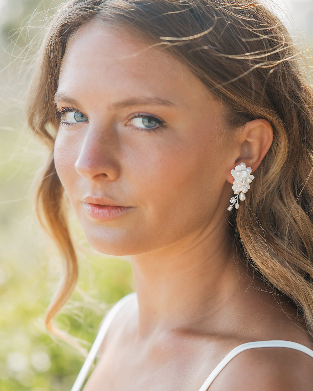 Bride with loose, sunlit waves wearing the Taylor ivory flower and pearl wedding earrings
