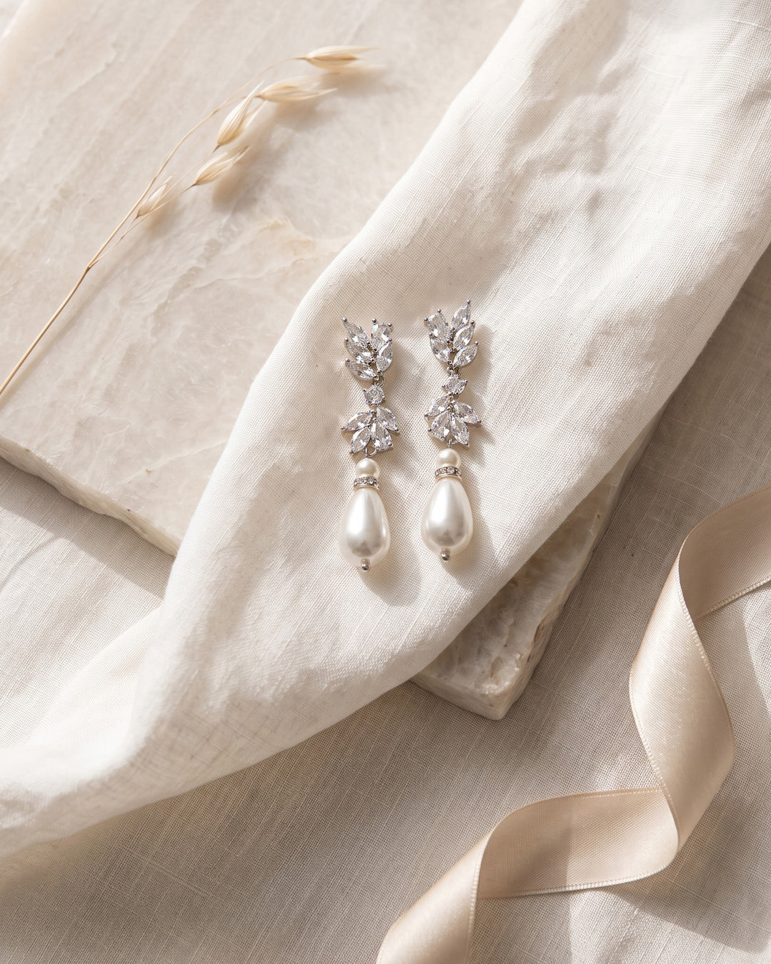 Jolene bridal earrings on linen and stone showing the teardrop pearls and CZ clusters up close