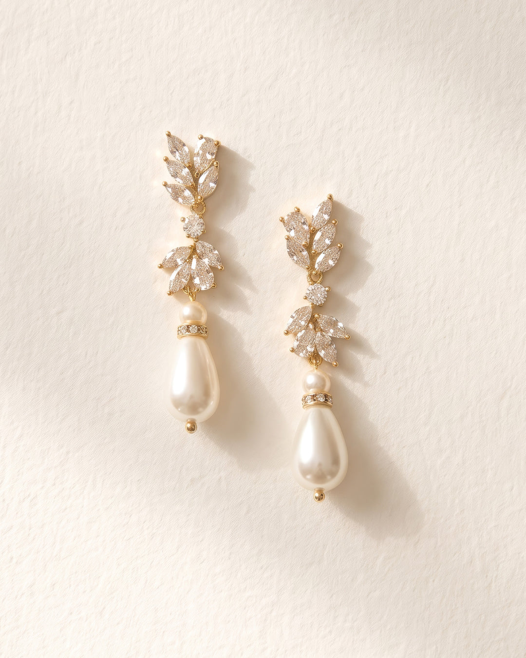 Gold Jolene teardrop pearl earrings with marquise CZ clusters on a soft cream background