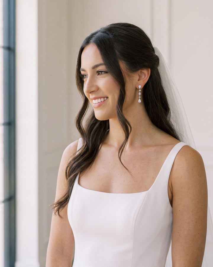 Smiling brunette bride with half-up waves and a veil wearing the Gracie wedding earrings