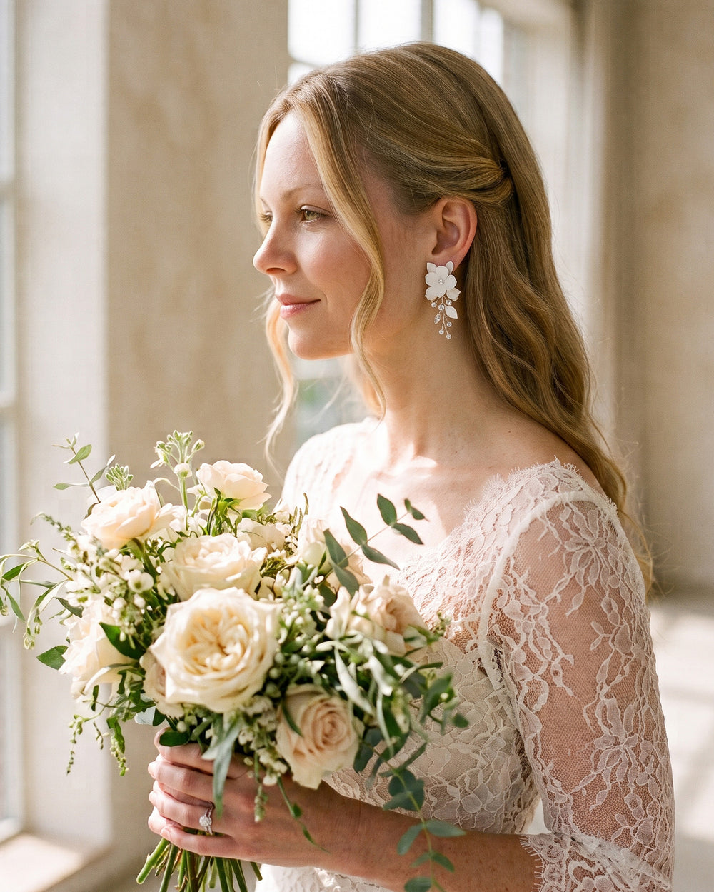 Bride in a lace gown holding cream roses and wearing Adeline flower earrings