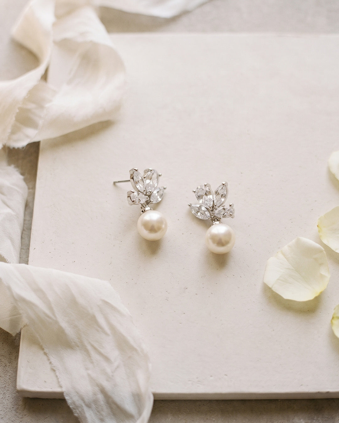 Syd bridal earrings laid on a cream board beside soft ribbon and petals