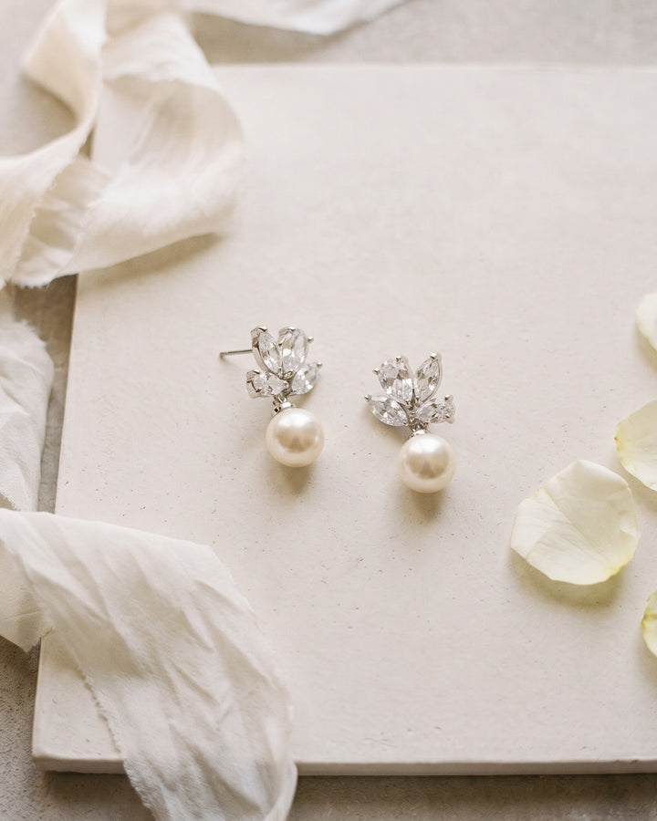 Syd bridal earrings laid on a cream board beside soft ribbon and petals