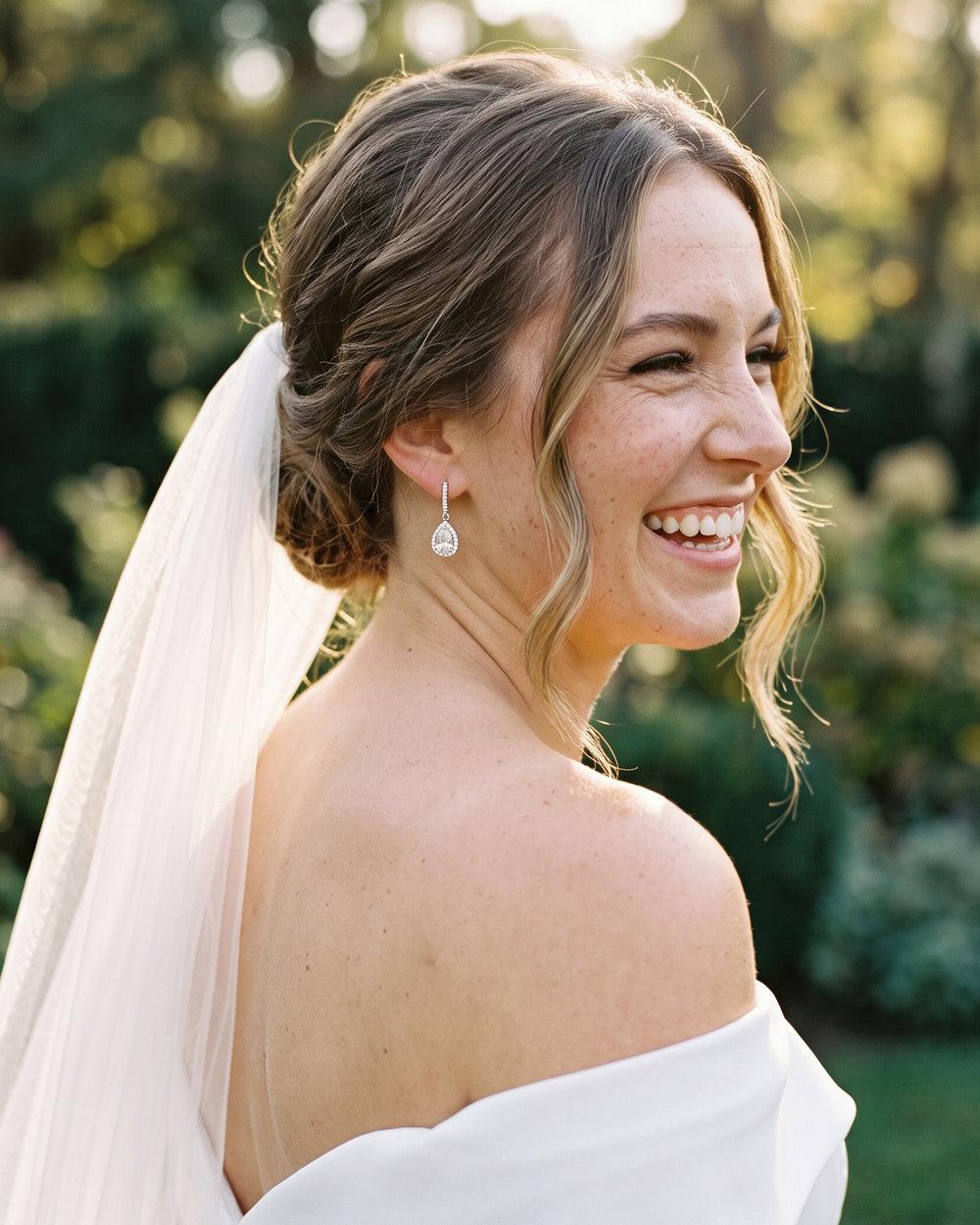 Laughing bride in a veil and off-the-shoulder gown wearing the Harper CZ wedding earrings