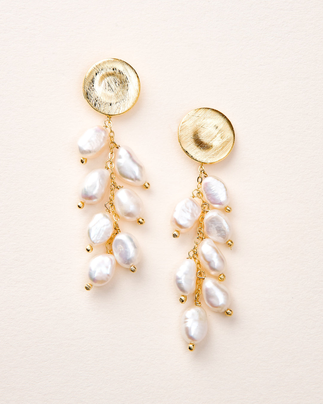 Pair of gold and pearl earrings on a light pink background
