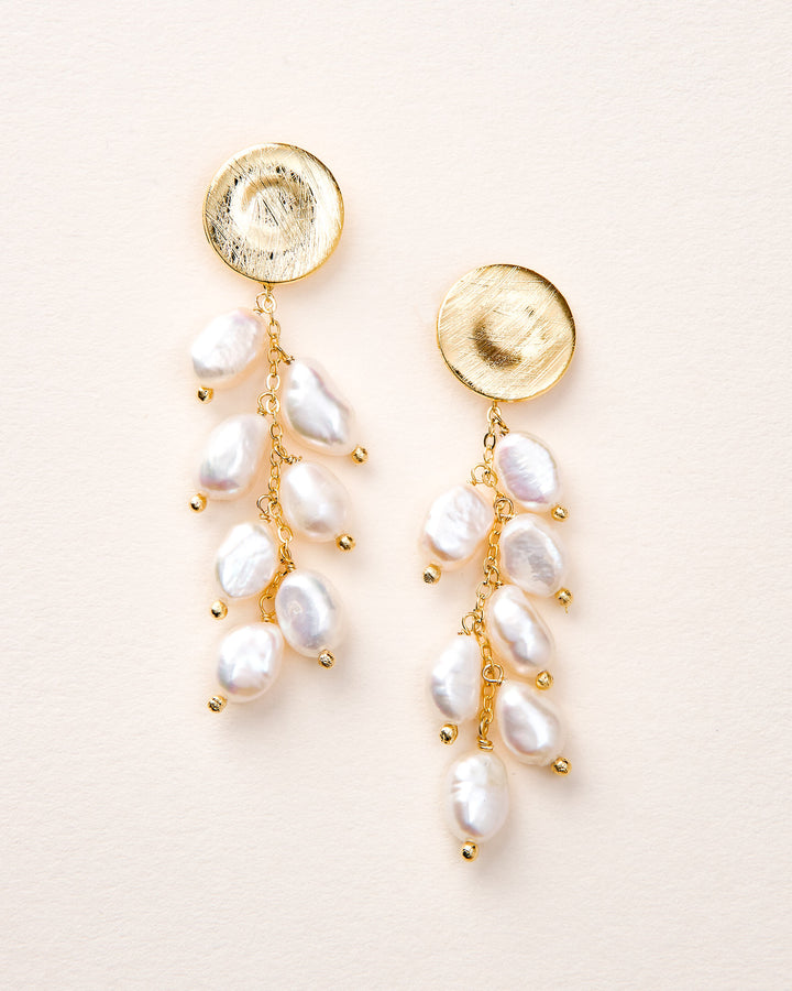 Pair of gold and pearl earrings on a light pink background