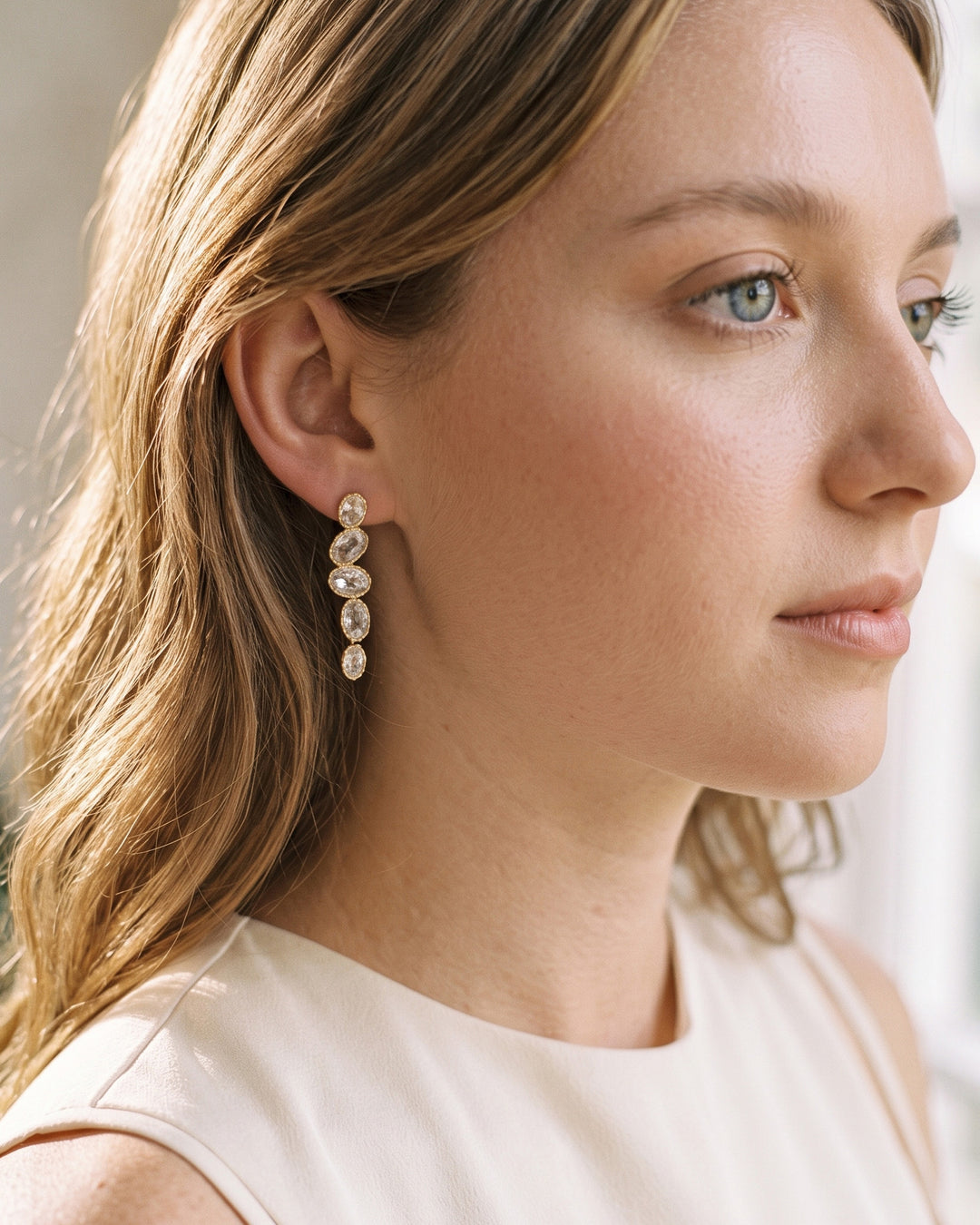Woman in a white sleeveless top wearing the Lisbon gold cubic zirconia drop earrings