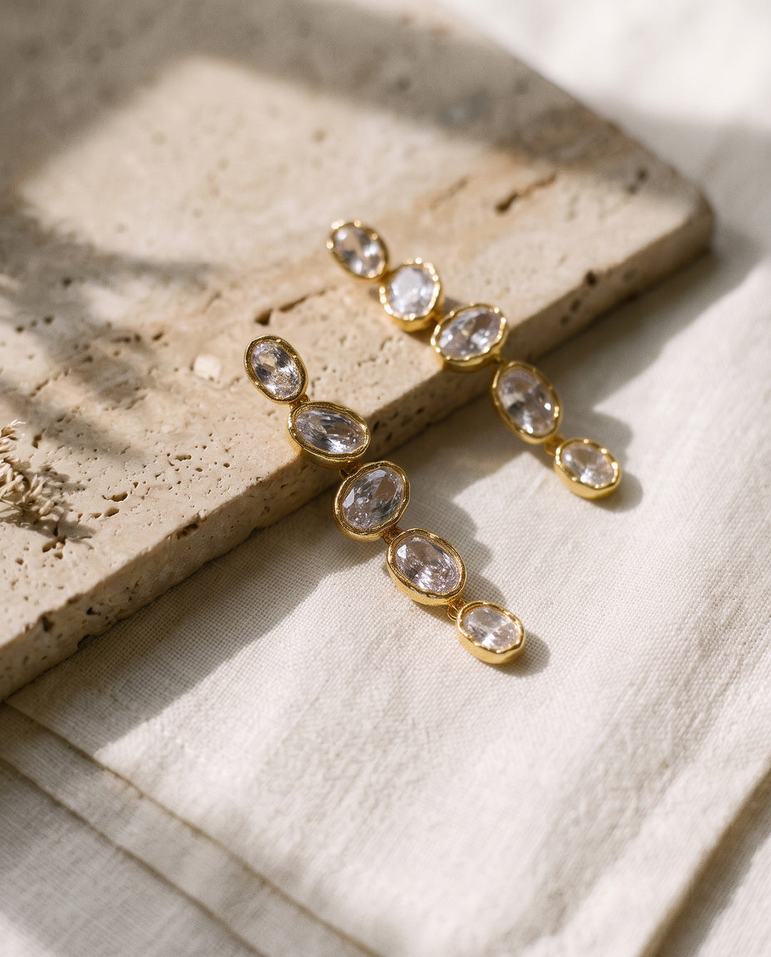Lisbon gold earrings on travertine stone and linen in soft sunlight