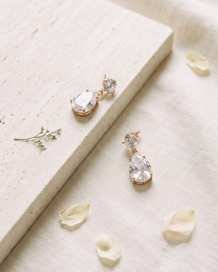 Gold Sia bridal earrings on travertine stone and ivory linen with petals