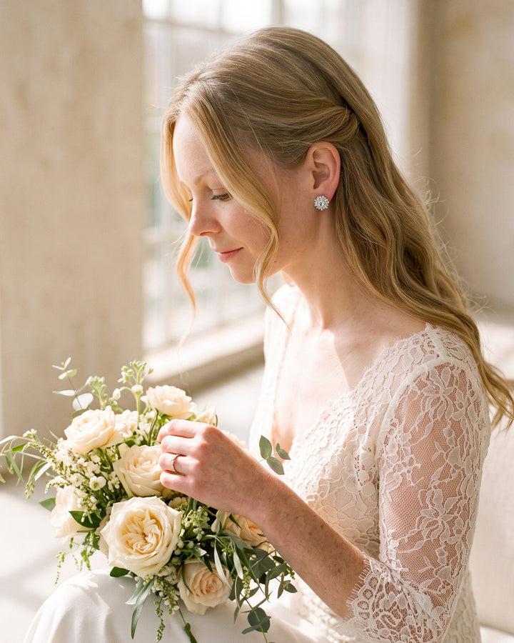Bride holding a rose bouquet by a sunlit window wearing Shivani CZ studs