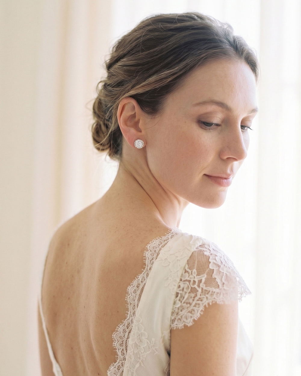 Bride wearing silver cubic zirconia sunburst stud earrings with a lace gown and soft updo