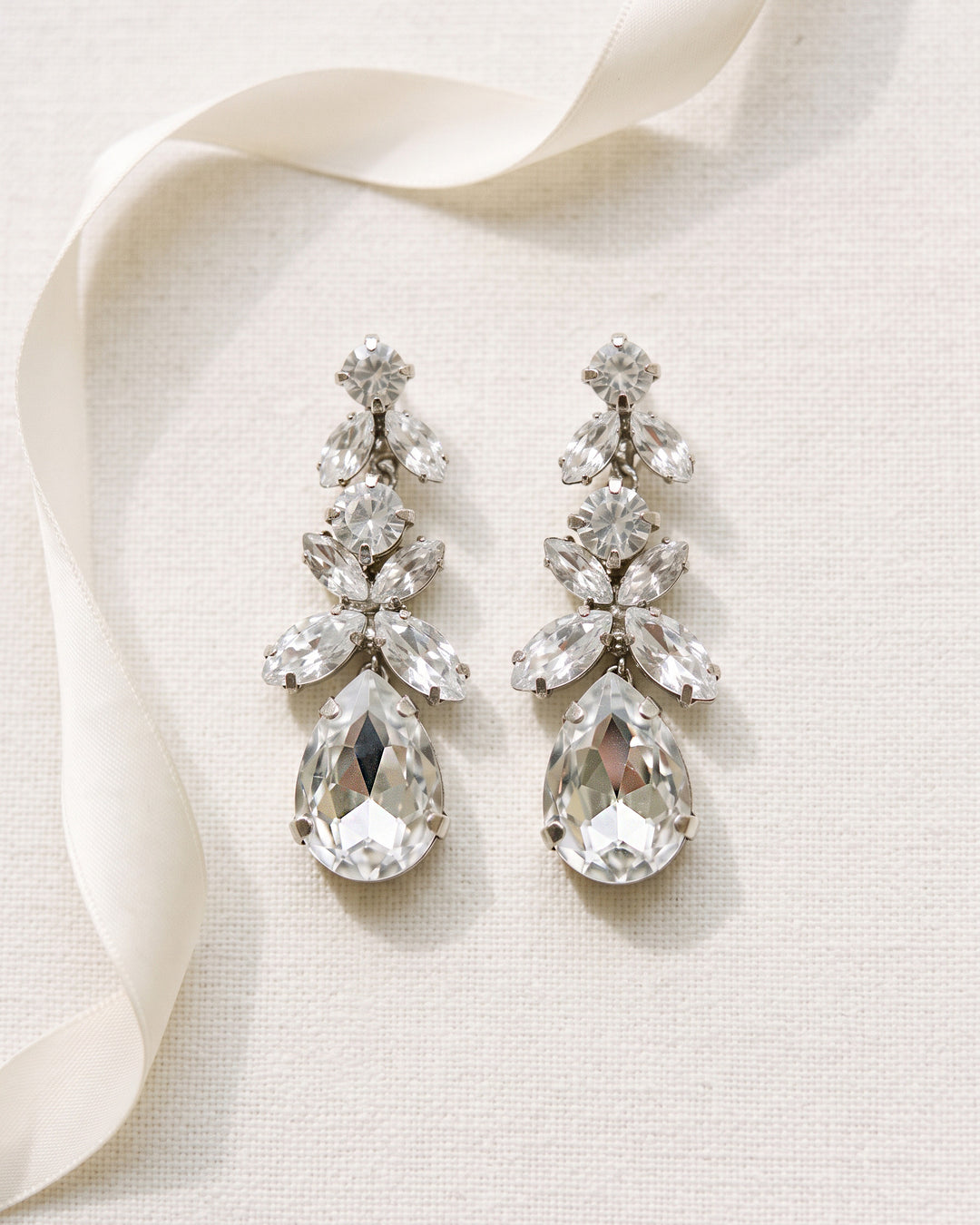 Pair of Tiana bridal earrings laid flat, marquise crystal clusters graduating down to a large teardrop crystal