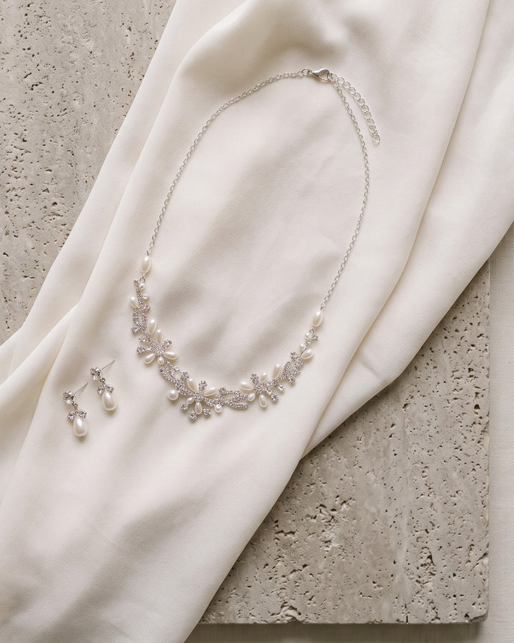 Delicate Pearl necklace and earrings laid on ivory silk over travertine stone